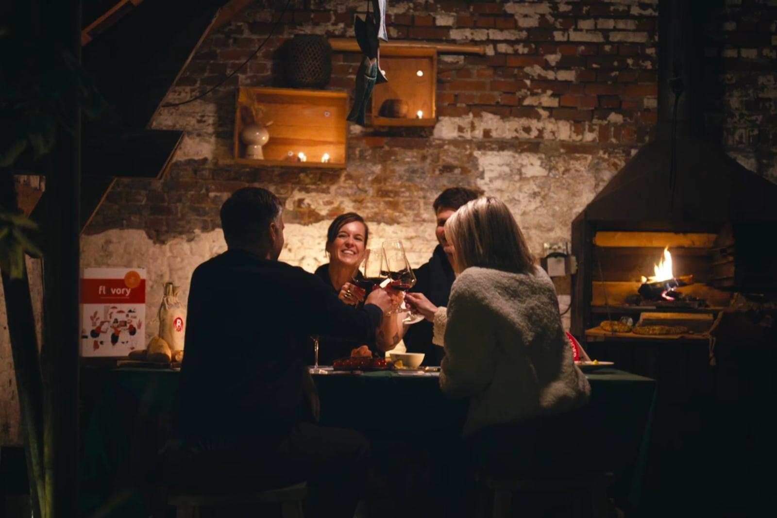 Vrienden klinken met rode wijn aan tafel bij het haardvuur tijdens een wijnproeverij thuis met Flavory
